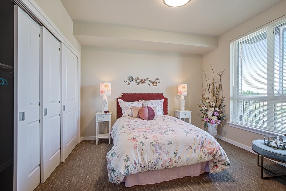 A cozy bedroom featuring a bed with floral patterned bedding, side tables with lamps, and large windows providing natural light.