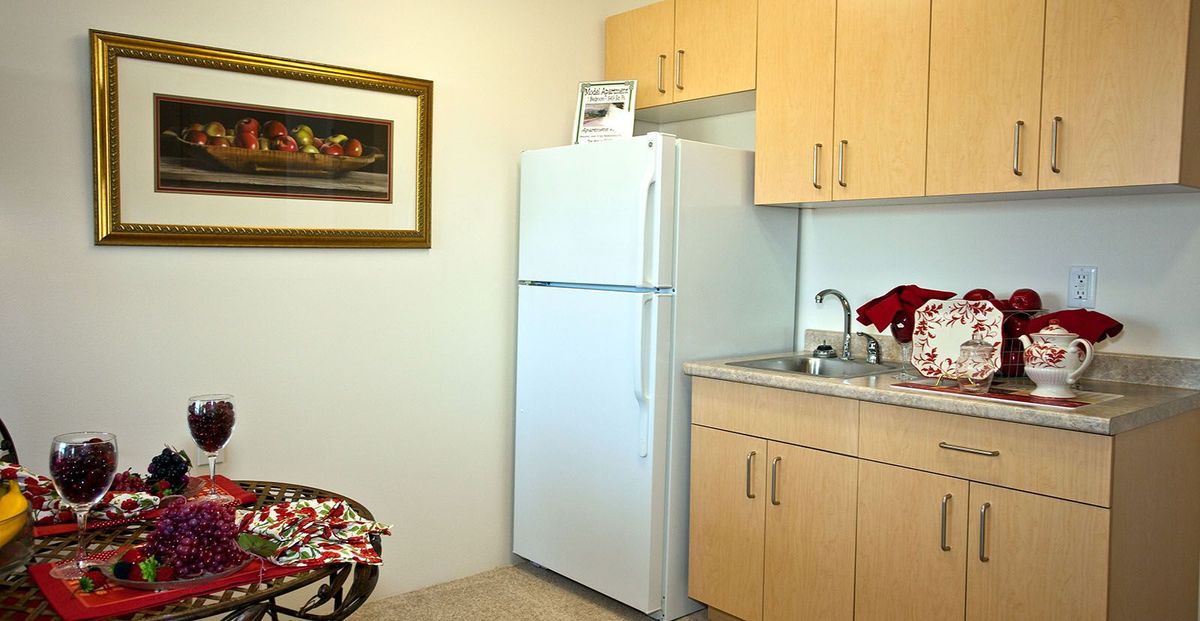 A small kitchen area with a refrigerator, sink, and wooden cabinets.