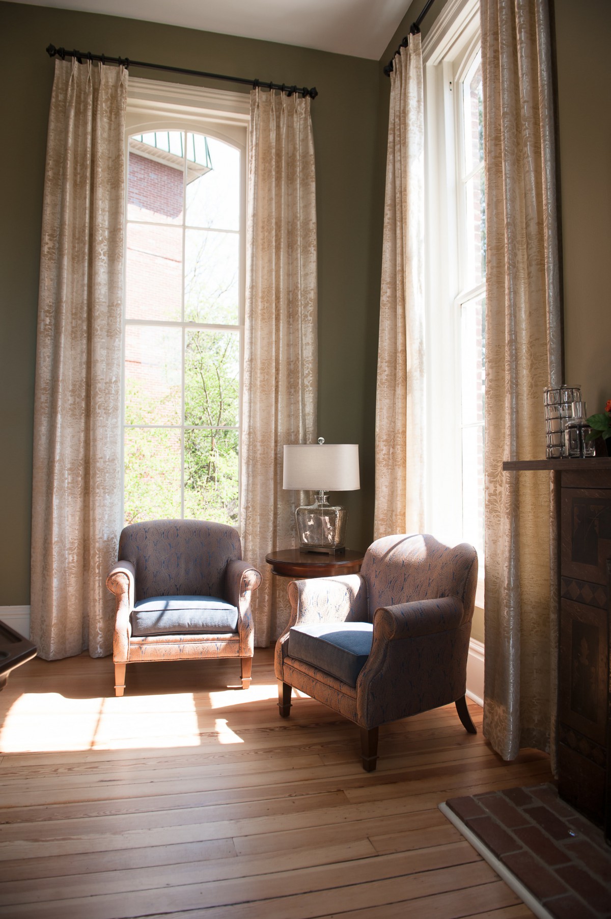 A cozy living room with two armchairs by a large window, adorned with curtains and a table lamp, basking in sunlight.
