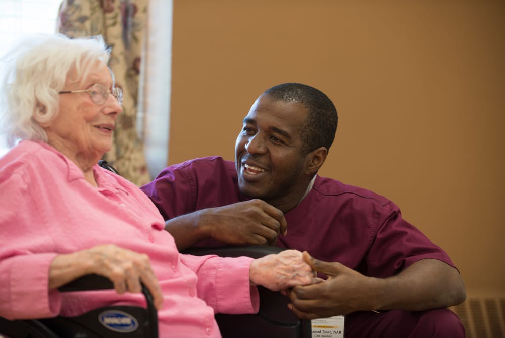 A caregiver smiling and holding hands with an elderly woman, showing compassion and support.