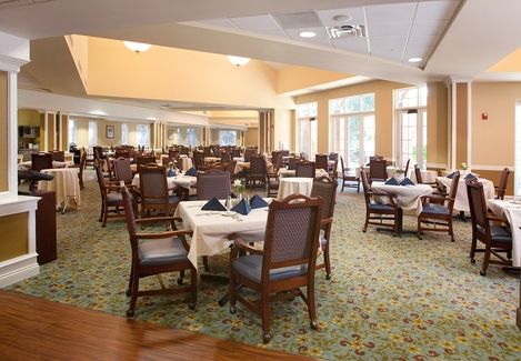 An elegant dining room with several tables and chairs neatly arranged, featuring a carpeted floor and ample natural light.