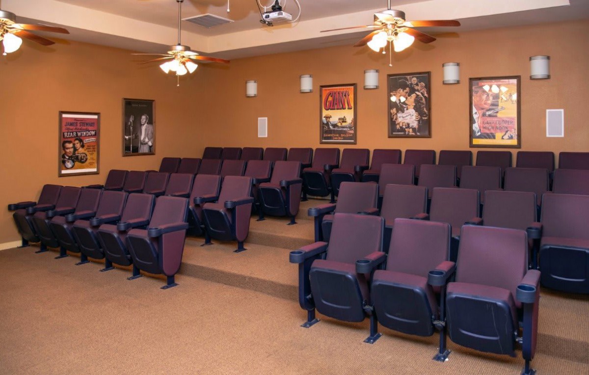 An empty home theater room featuring purple seating, movie posters on the walls, and ceiling fans overhead.