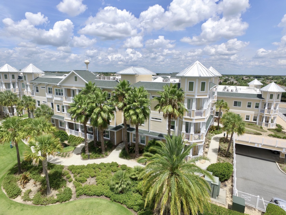 A picturesque view of a residential building surrounded by palm trees under a cloudy sky.