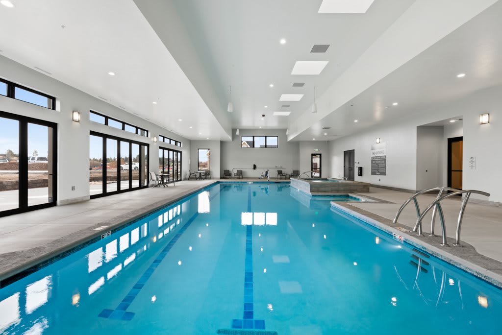 A modern indoor swimming pool with large windows and bright lighting.