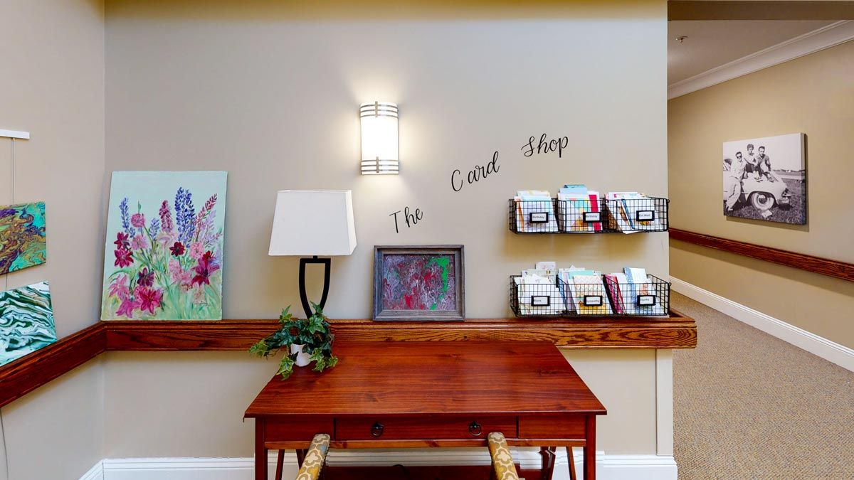 A cozy reading nook featuring a wooden desk, wall-mounted lamp, artwork, and a small bookshelf.