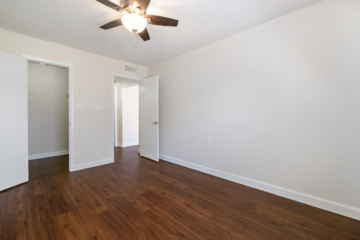 An empty room with wooden flooring, a ceiling fan, and white walls.