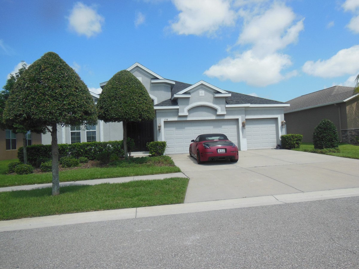 A suburban house with a car parked in the driveway under a partly cloudy sky.