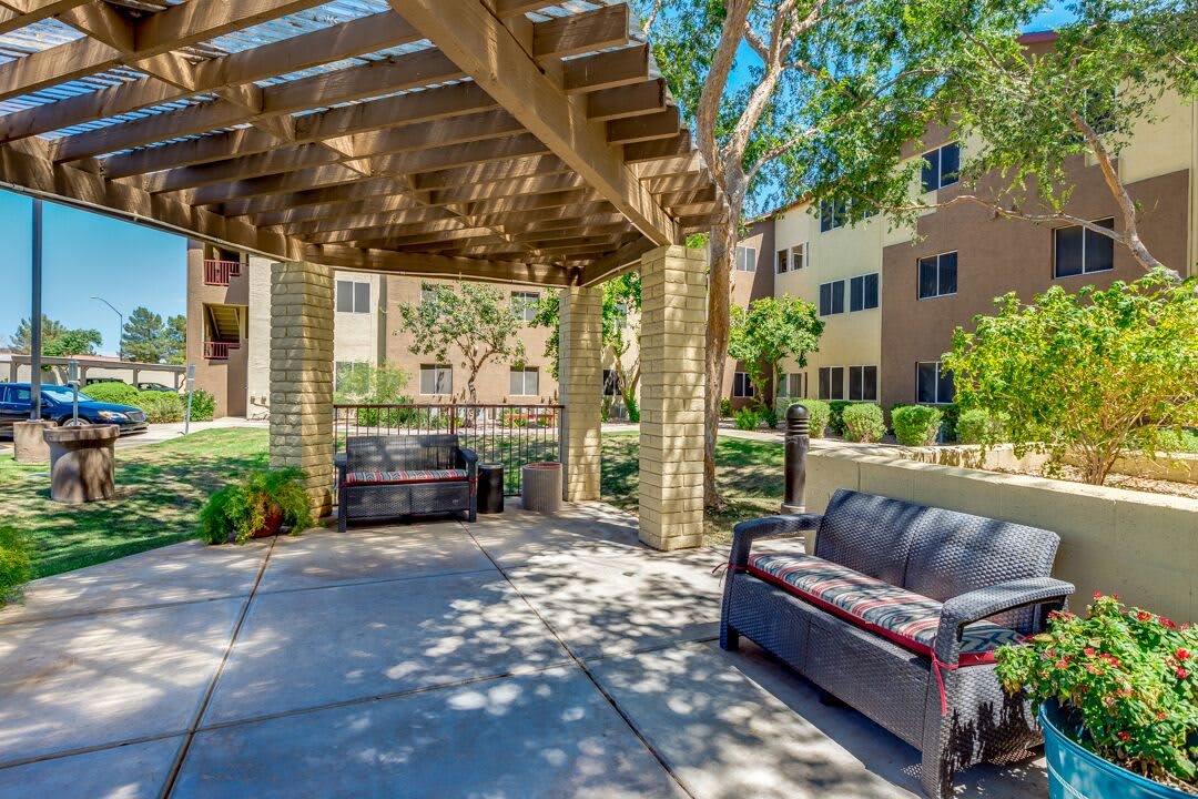 A shaded outdoor seating area with patio furniture under a pergola in an apartment complex garden.