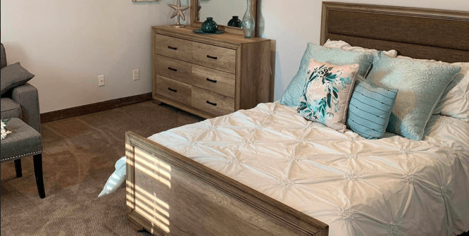 A cozy bedroom with a wooden bed and dresser, decorated with elegant bedding and pillows.