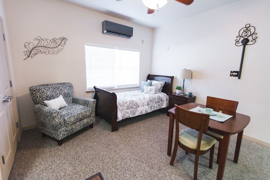 A cozy bedroom with a bed, armchair, and dining table set near a window.