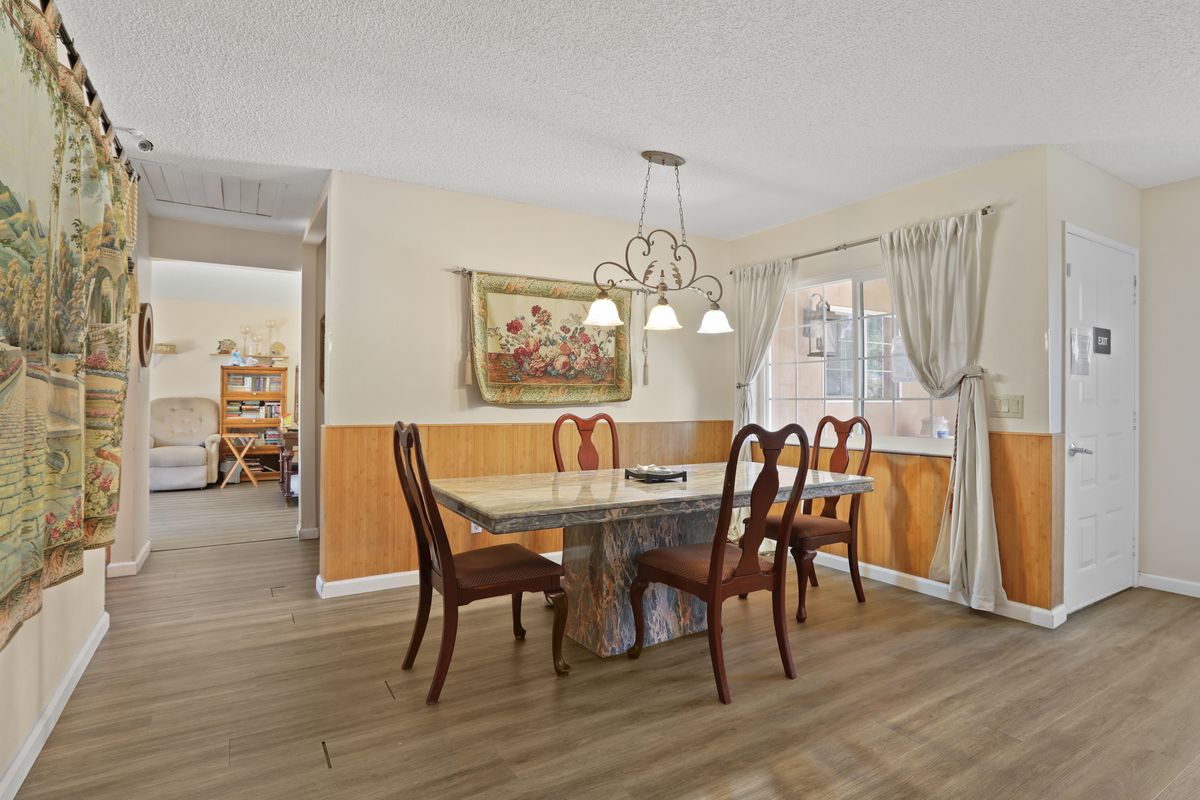 A cozy dining room with a wooden table and chairs, enhanced by a chandelier and curtains.