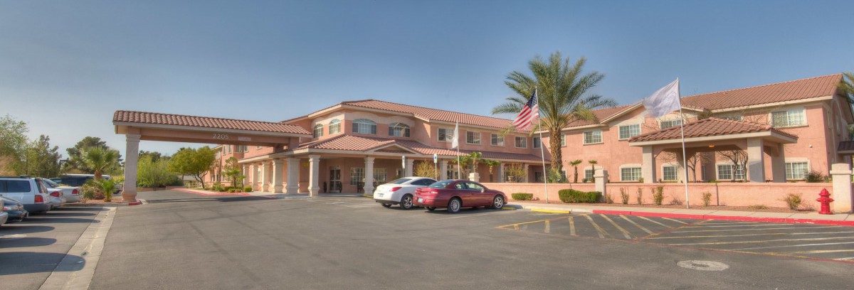 A two-story building with a parking lot, palm trees, and an American flag on a sunny day.
