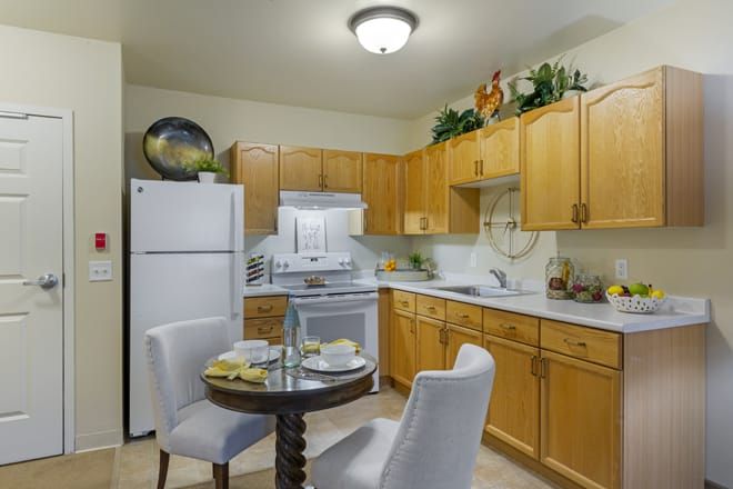 A cozy kitchen with wooden cabinets, white appliances, and a small dining table set for two.