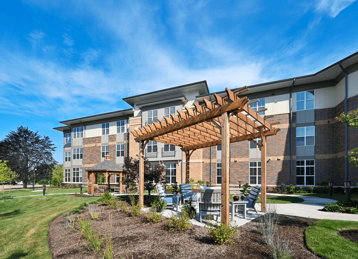 A modern apartment building with a wooden pergola and outdoor seating area under a clear blue sky.