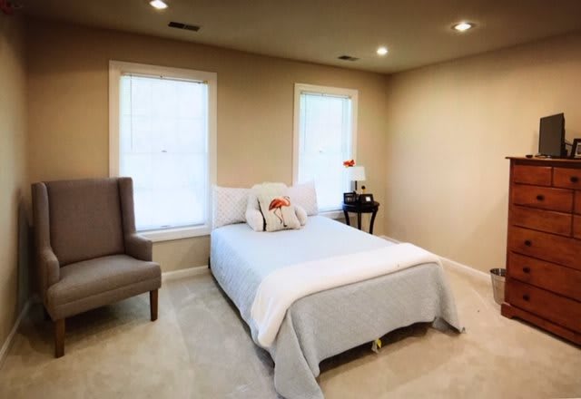 A cozy and minimalist bedroom featuring a comfortable bed, armchair, and two large windows.