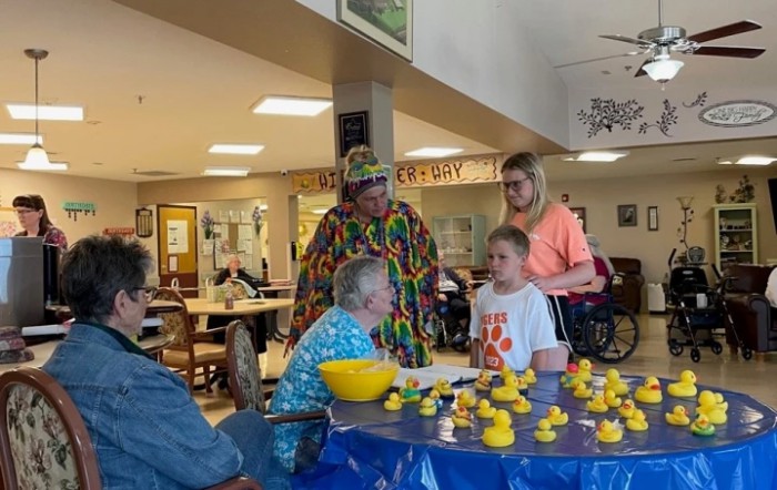 A group of people enjoying a community event indoors, gathered around a table with rubber ducks.