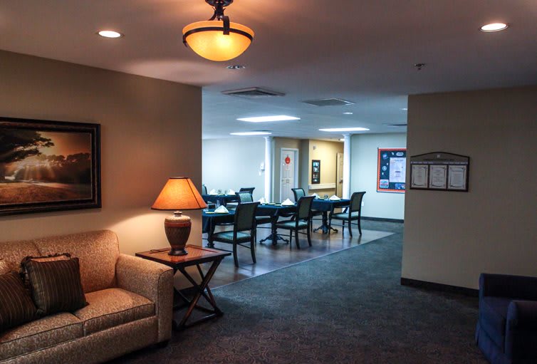 A cozy interior space featuring a seating area with a sofa and lamp, leading into a dining area.