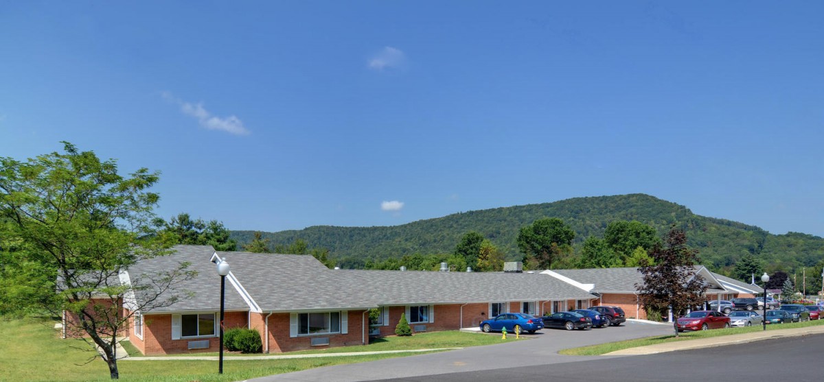 A view of a motel surrounded by mountains with cars parked in front.