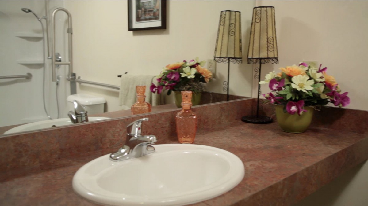A bathroom countertop with a sink, decorated with flowers and lamps.