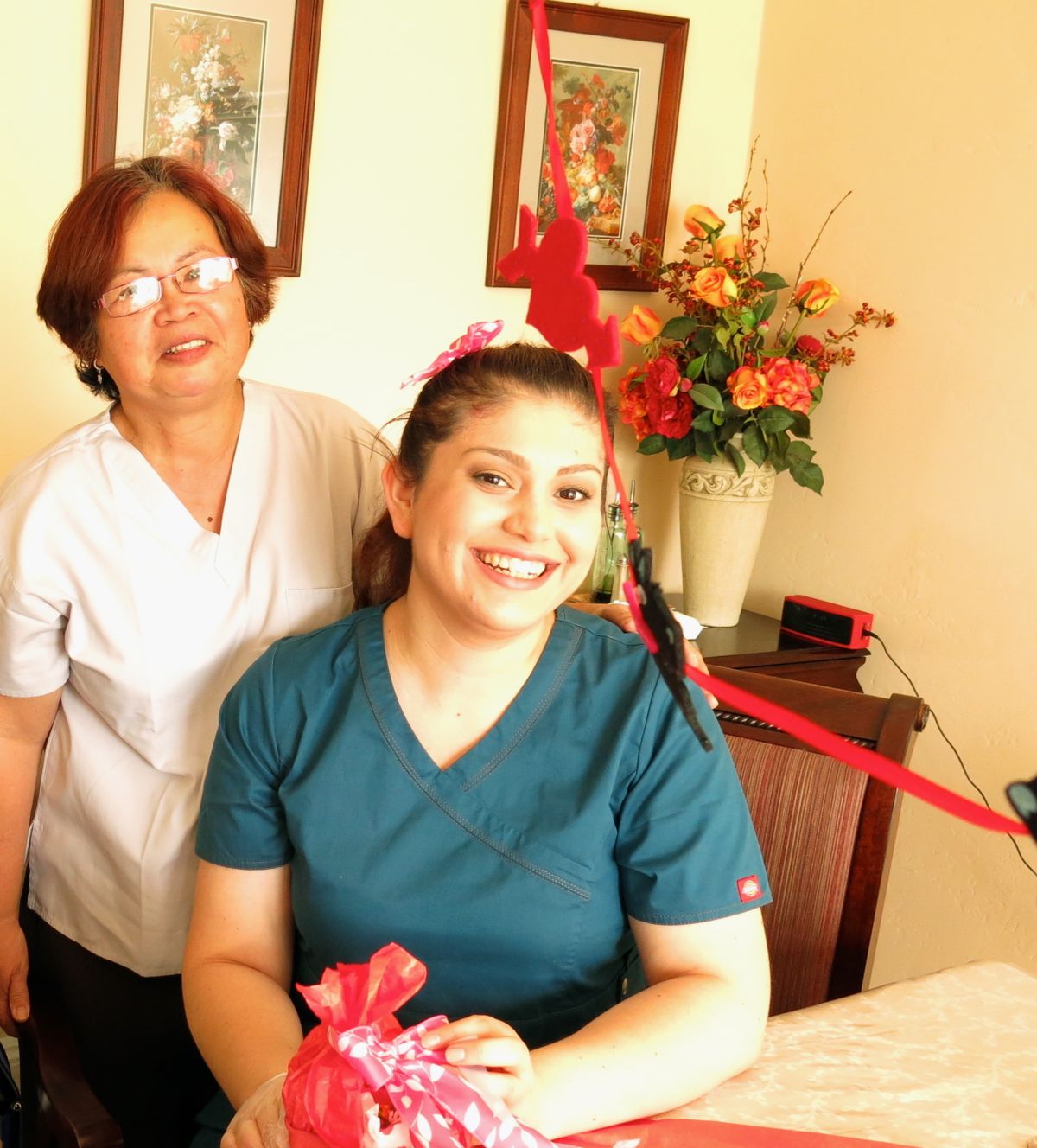 Two women indoors, one smiling and holding a gift.