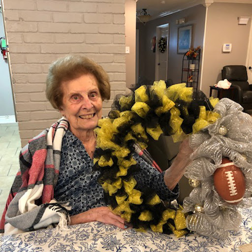 A cheerful elderly woman proudly displays her handmade football-themed wreath.