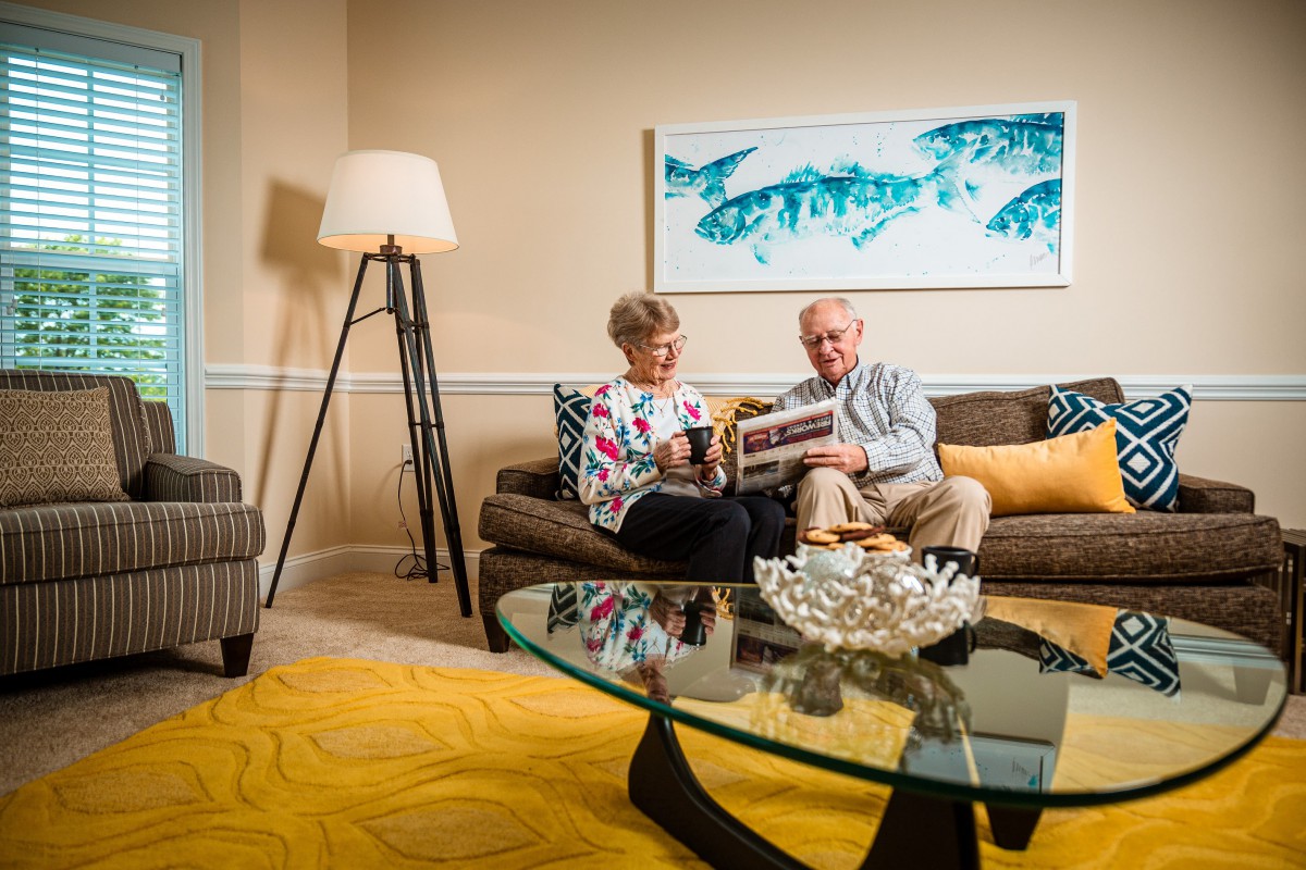 A couple sitting on a sofa in a well-decorated living room, reading together.