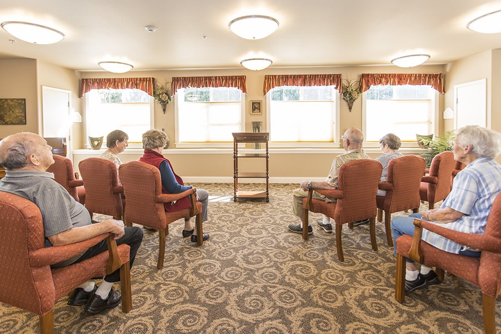 A group of elderly people seated in a community room setting.