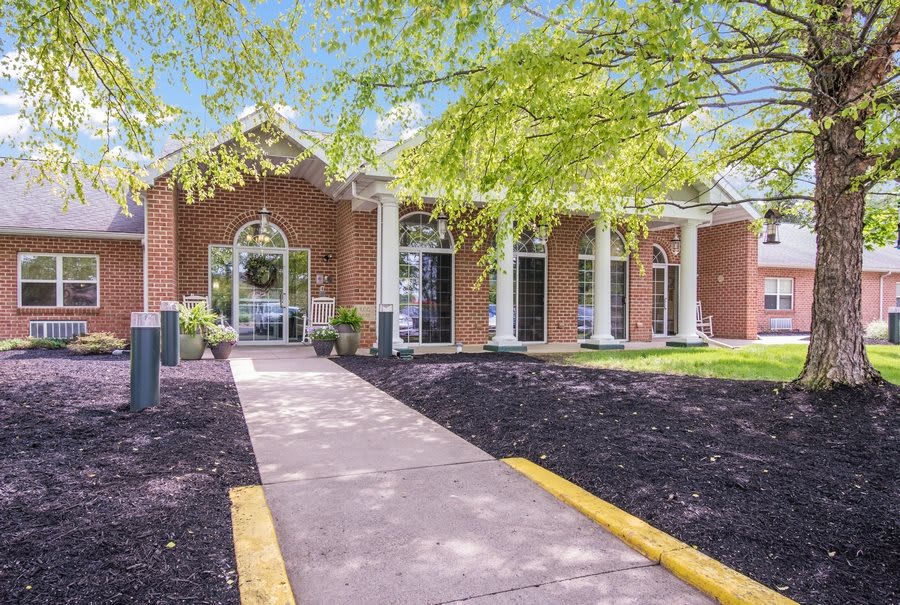 A brick building with columns and a landscaped entrance.