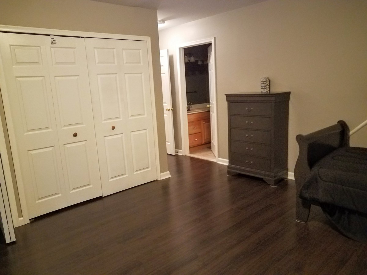 A clean, empty room with wood flooring and a dresser beside a closet.