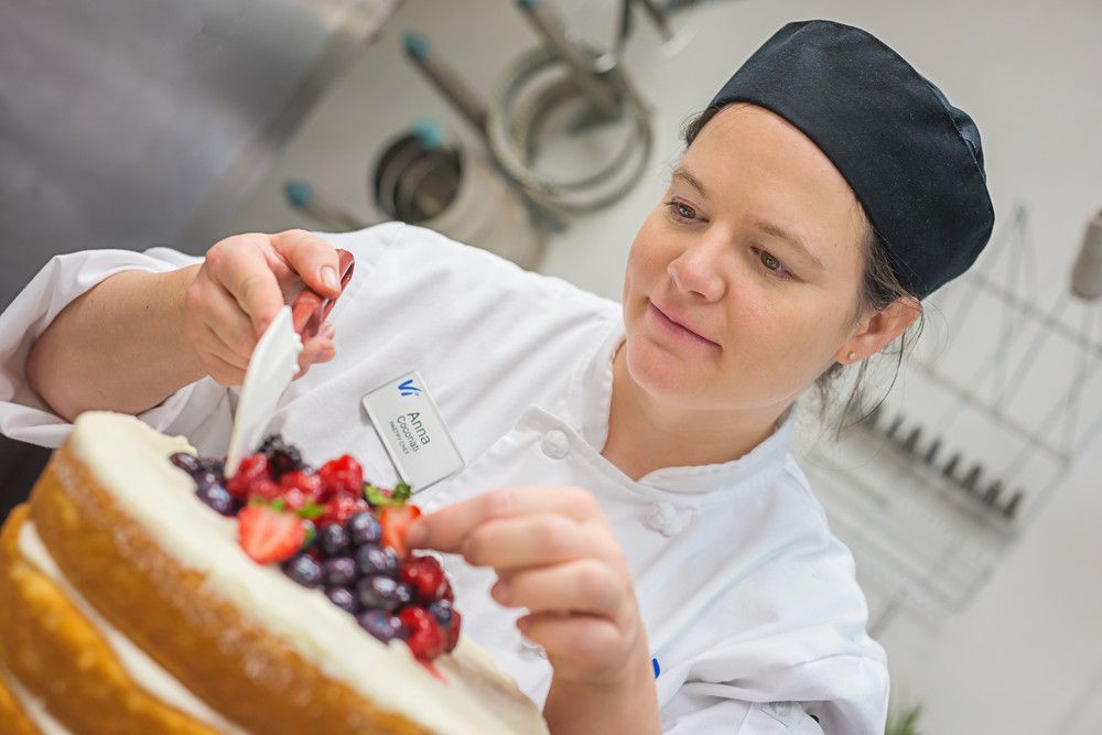 A chef decorating a cake with fresh fruits in a kitchen.