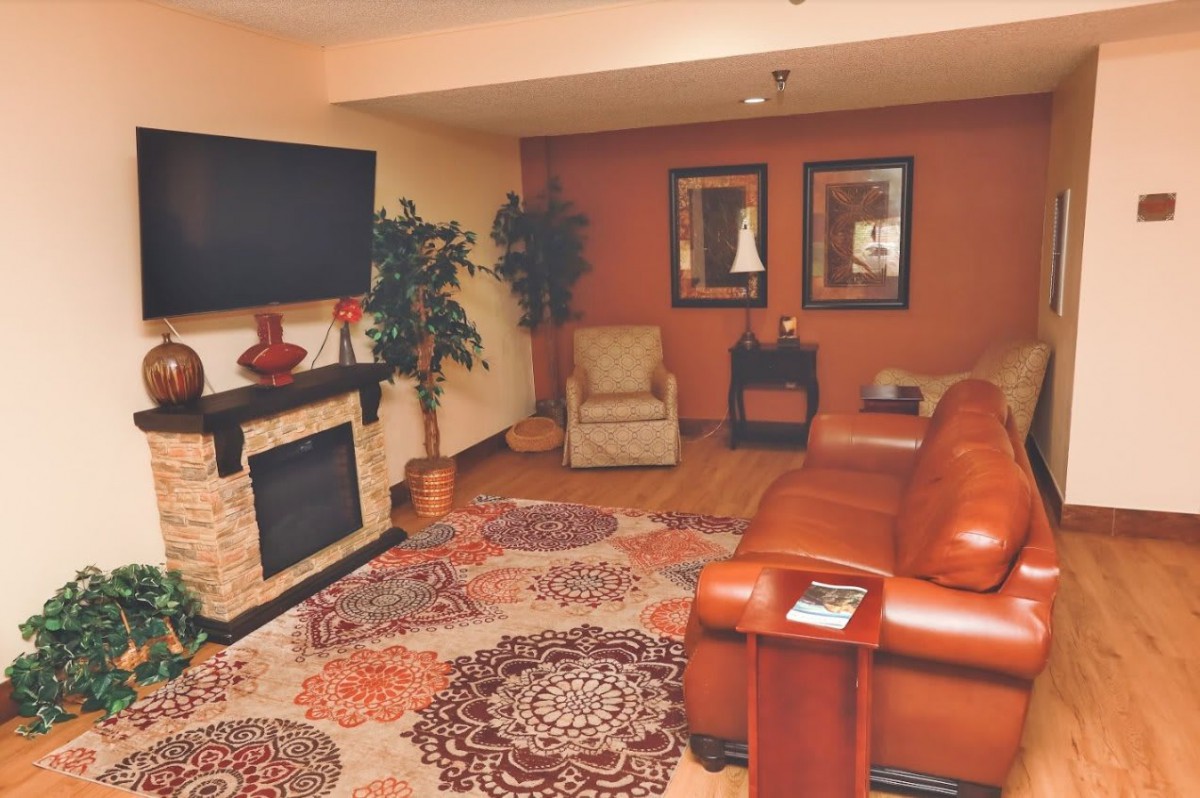 A cozy living room with a leather sofa, patterned rug, and a wall-mounted TV above the fireplace.