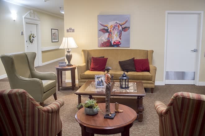 A cozy living room featuring a sofa, various chairs, and a coffee table adorned with decorative items. A colorful cow painting hangs on the wall, adding a playful touch to the space.