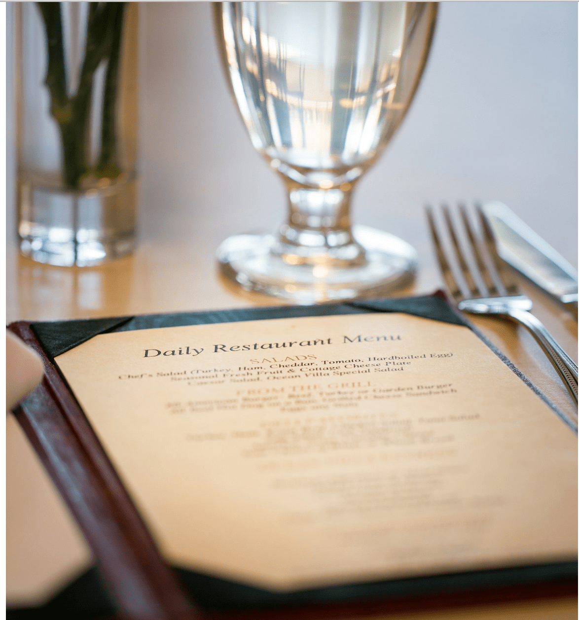 A close-up of a restaurant menu placed on a table with a glass of water and cutlery.