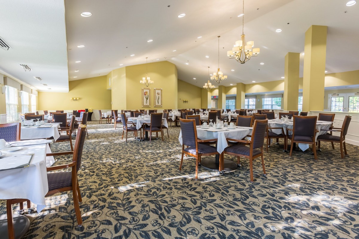 An elegant dining room with neatly arranged tables and chairs, featuring chandeliers and a patterned carpet.