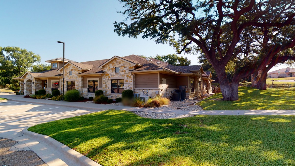 A beautiful stone house with well-maintained landscaping and a large tree in the front yard.