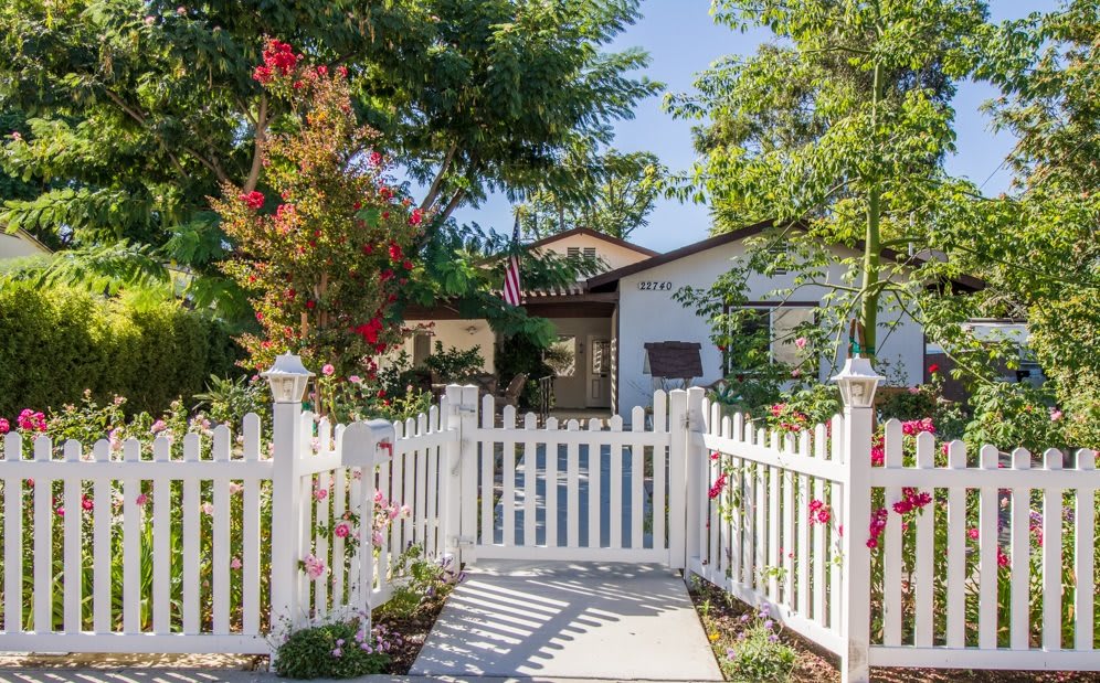 A charming house with a white picket fence, surrounded by lush trees and vibrant flowers.