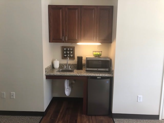 A small kitchenette area with cabinets, sink, refrigerator, and microwave.