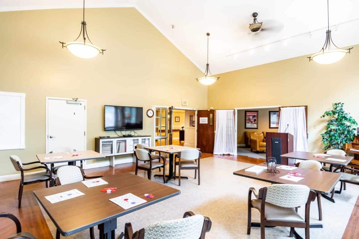 A bright and airy dining room featuring several tables and chairs, a television, and warm lighting.