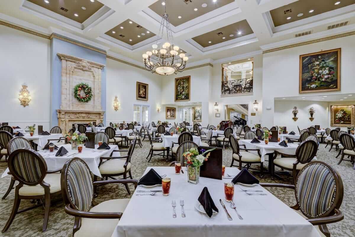 An elegant restaurant dining room with formal table settings and chandeliers.