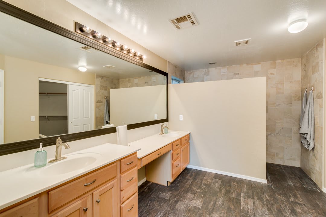 A modern bathroom featuring a double vanity with wooden cabinets and large mirror, accented by overhead lighting and tile flooring.