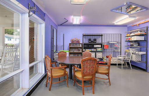 A cozy and inviting room designed for reading and gatherings, featuring a round table surrounded by wicker chairs against a soft purple backdrop.