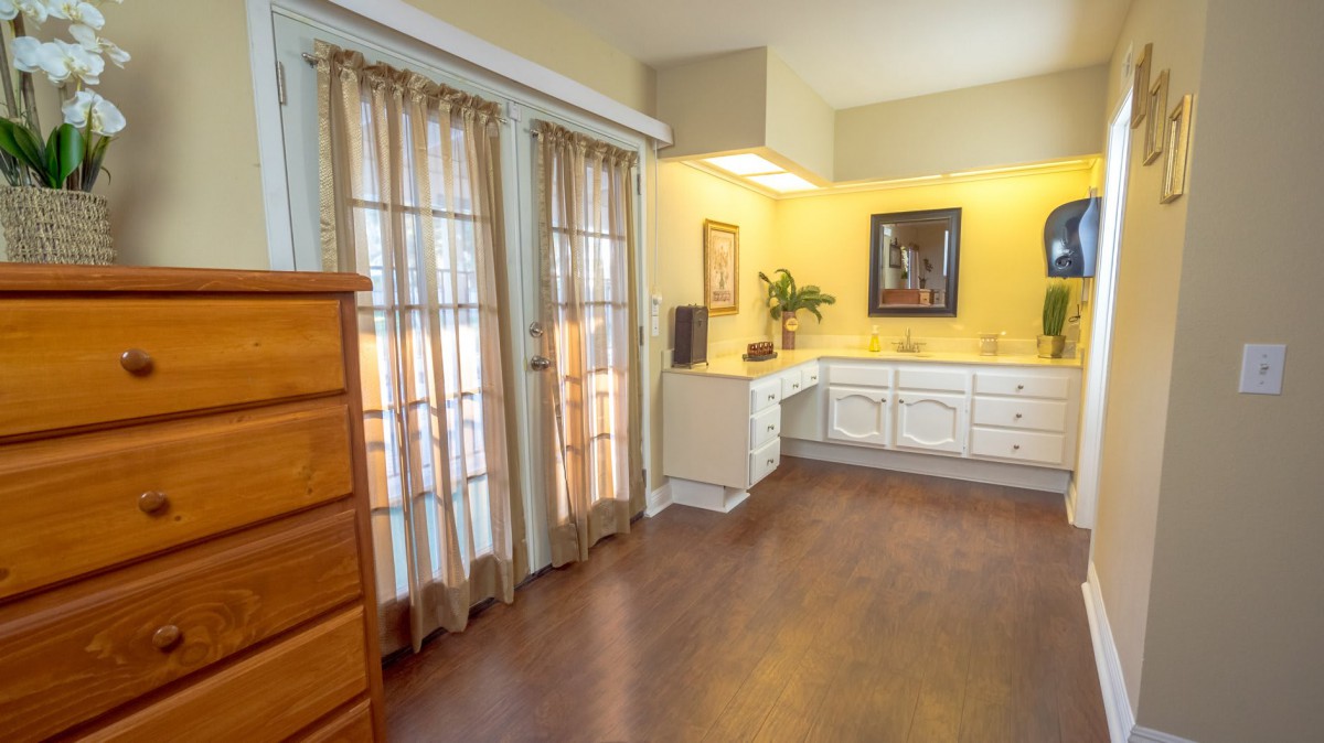 A cozy room with wooden flooring, featuring a dresser, curtains, and a cabinet with decorative items.