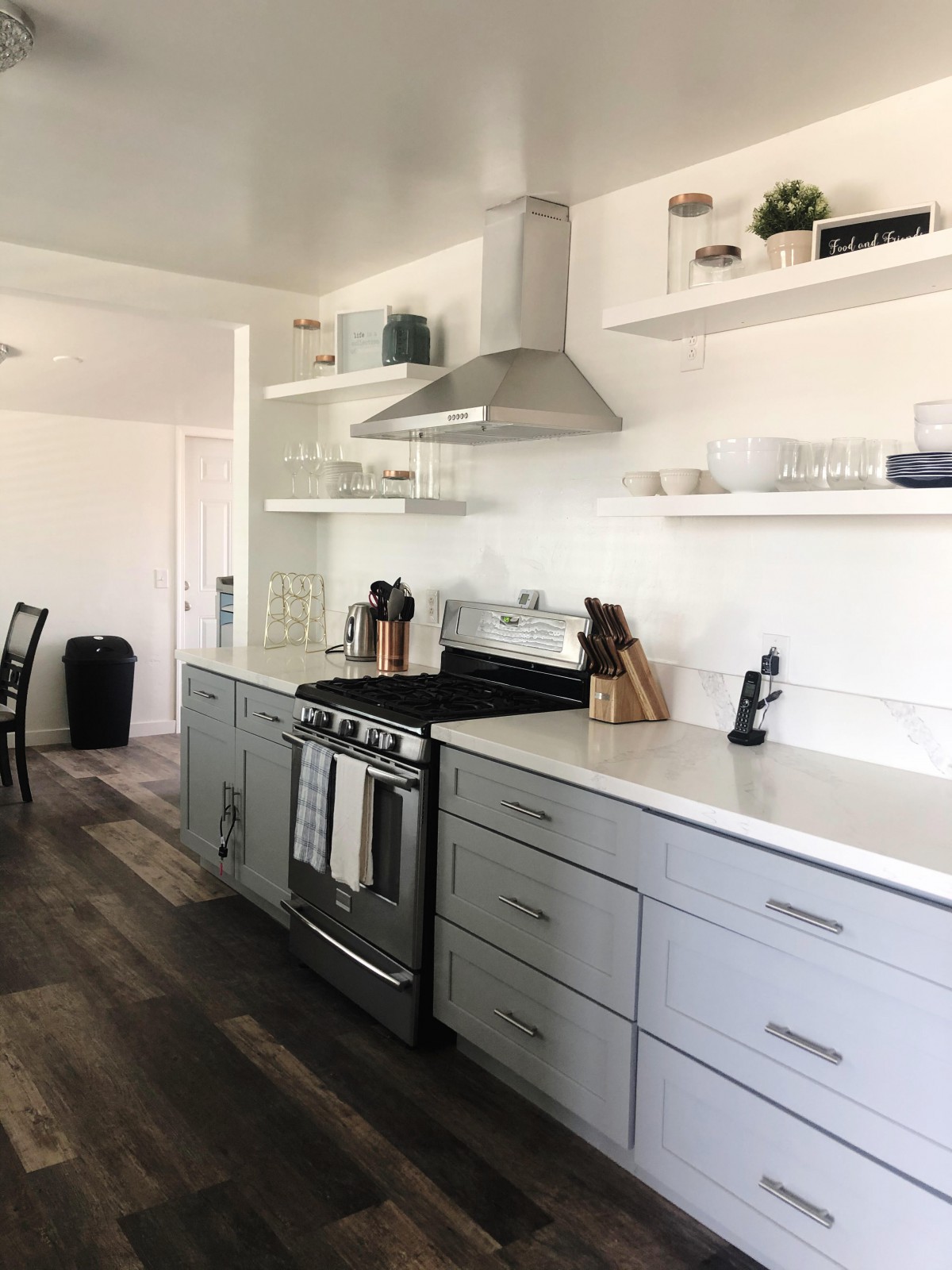 A modern kitchen with white cabinetry, stainless steel appliances, and open shelving.