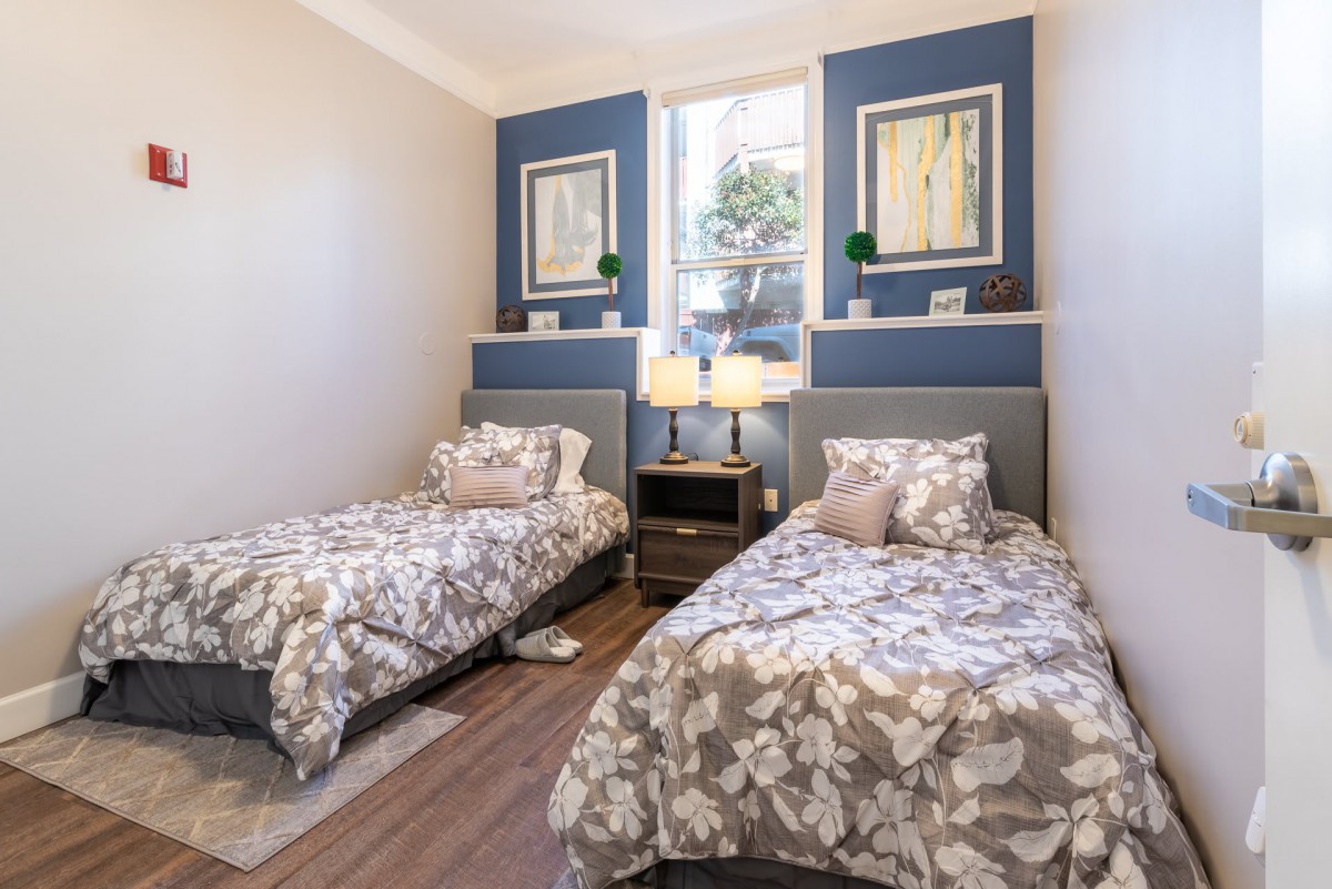 A cozy bedroom featuring twin beds with floral bedding, complemented by elegant wall art and a centrally placed nightstand with lamps.