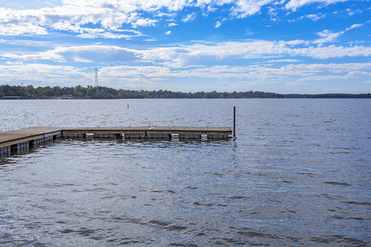 A serene lake with a floating dock under a partly cloudy sky.