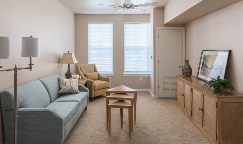 A cozy living room with a sofa, armchair, nesting tables, and soft lighting.