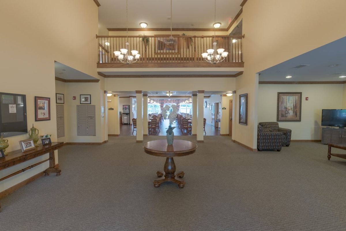 A spacious lobby area featuring chandeliers, a central table, and an upper balcony.