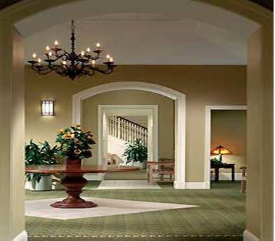 A beautifully decorated hallway featuring a central table with plants, elegant chandeliers, and an inviting staircase.