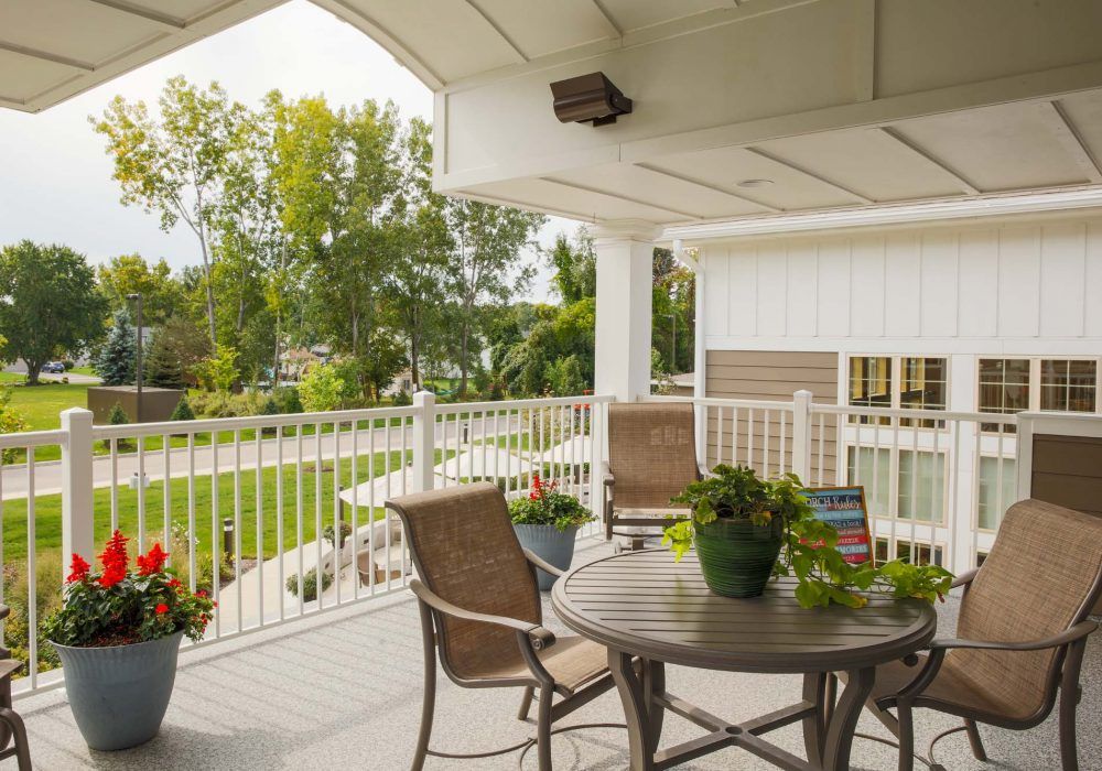 A cozy porch with a table and chairs overlooking a lush garden.