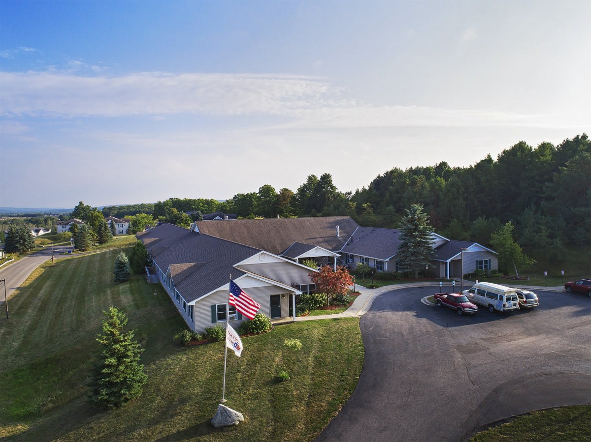 Aerial view of a building surrounded by greenery with flags at the entrance and a parking area.